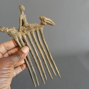 May include: A bronze comb with a figure of a person riding a stylized animal. The comb has eight teeth and is decorated with intricate details.