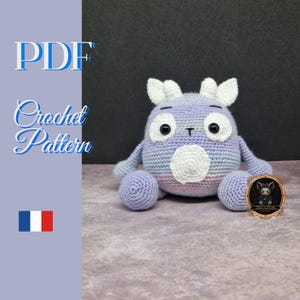 May include: A crochet pattern for a purple and white amigurumi monster with big eyes and a white nose. The pattern is available as a PDF download.