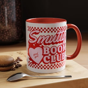 May include: White ceramic mug with a red interior and handle. The mug features the text "Smutty Book Club" in a retro font, with a heart graphic that says "good girl". The design is set against a red and white checkered pattern.