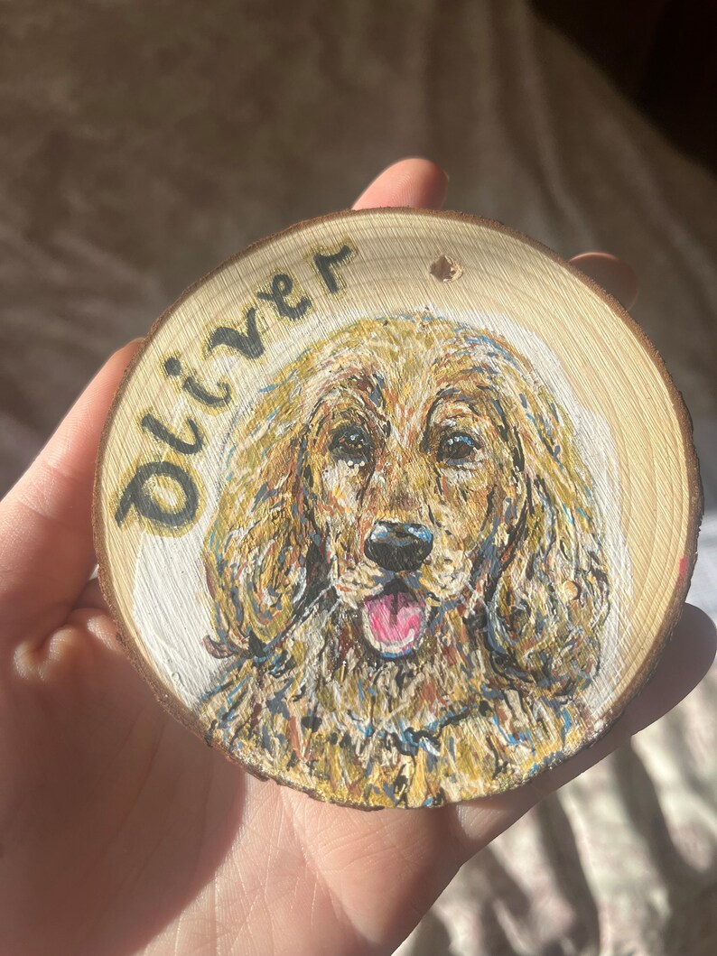 May include: A wooden round ornament with a painted portrait of a golden dog with the name "Oliver" written on the top.
