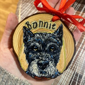 May include: A wooden ornament with a hand-painted portrait of a black dog with white markings. The dog's name, "Bonnie", is written in gold lettering on the ornament.