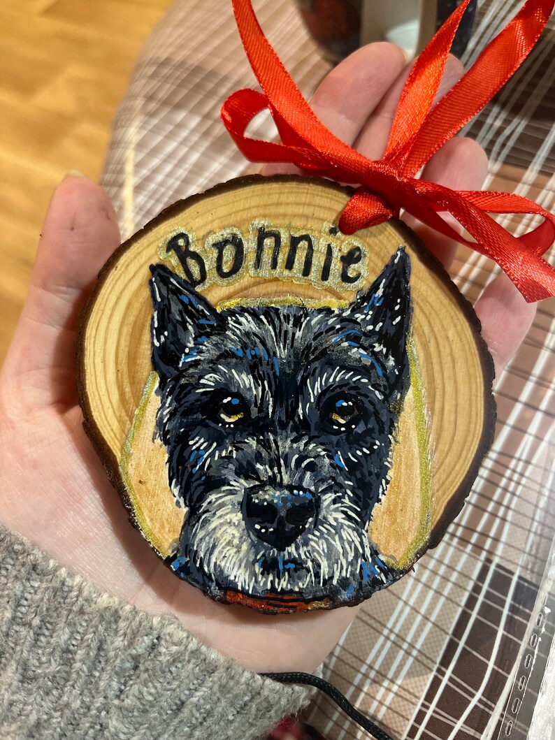 May include: A wooden ornament with a hand-painted portrait of a black dog with white markings. The dog's name, "Bonnie", is written in gold lettering on the ornament.