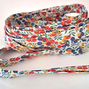 Può includere: Un rotolo di sbieco floreale con sfondo bianco, ornato da un motivo di fiori rossi, blu e gialli e foglie verdi. Il nastro è arrotolato, con una parte che si estende verso l'esterno. Questo bordo in tessuto è adatto per progetti di cucito e artigianato.