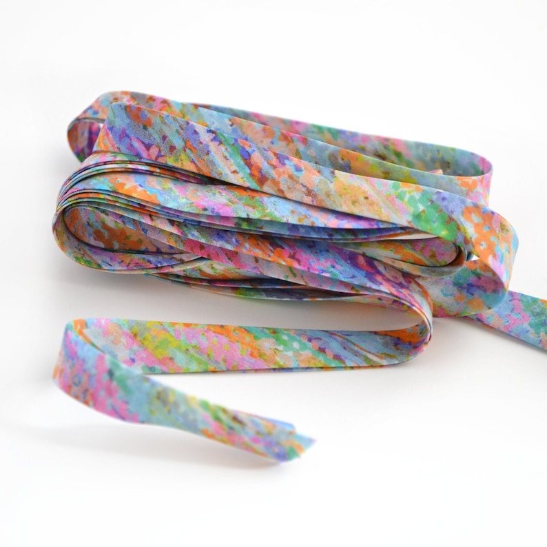 May include: A coiled length of fabric ribbon featuring a vibrant, multi-coloured abstract pattern. The design consists of blended strokes of light blue, bright orange, soft pink, and lime green, creating a textured, painterly appearance throughout.