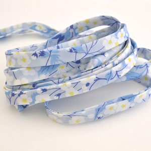 May include: A length of floral fabric trim, featuring a light blue background with white and yellow flower patterns. The trim is folded and coiled, showcasing the detailed design and color palette. Ideal for sewing and crafting projects.
