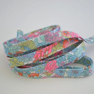 May include: A coiled length of floral patterned fabric ribbon. The ribbon features a repeating pattern of pink, blue, yellow, and orange flowers and leaves on a white background. The ribbon is likely used for crafting or decorative purposes.