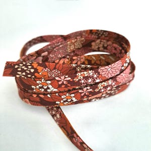Peut inclure: Un rouleau de ruban en tissu marron avec un imprimé floral dans les tons orange, rose et blanc.