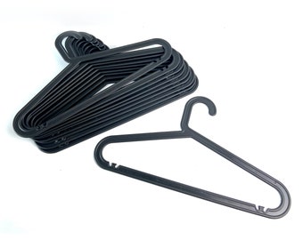 May include: A collection of black plastic clothes hangers. The hangers have a simple design with a curved hook and a wide bar for supporting garments. The hangers are stacked together, with one hanger separate.