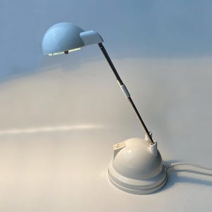 Può includere: Una lampada da tavolo bianca con un paralume a cupola e un braccio flessibile. La lampada ha un cavo bianco e una base bianca.