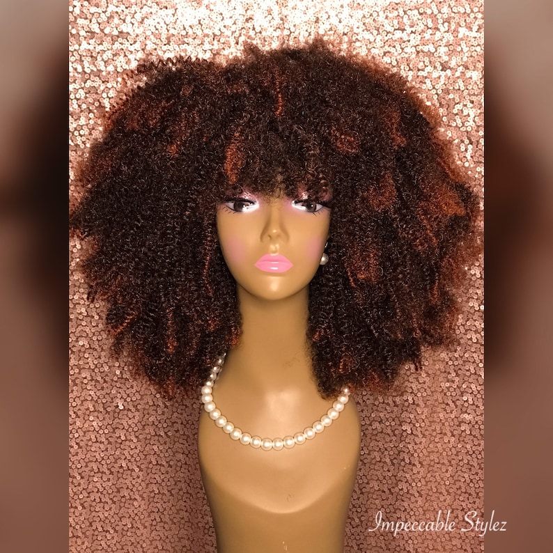 Puede incluir: Una peluca afro marr&oacute;n con flequillo en una cabeza de maniqu&iacute;. La peluca tiene un ligero tono marr&oacute;n rojizo.