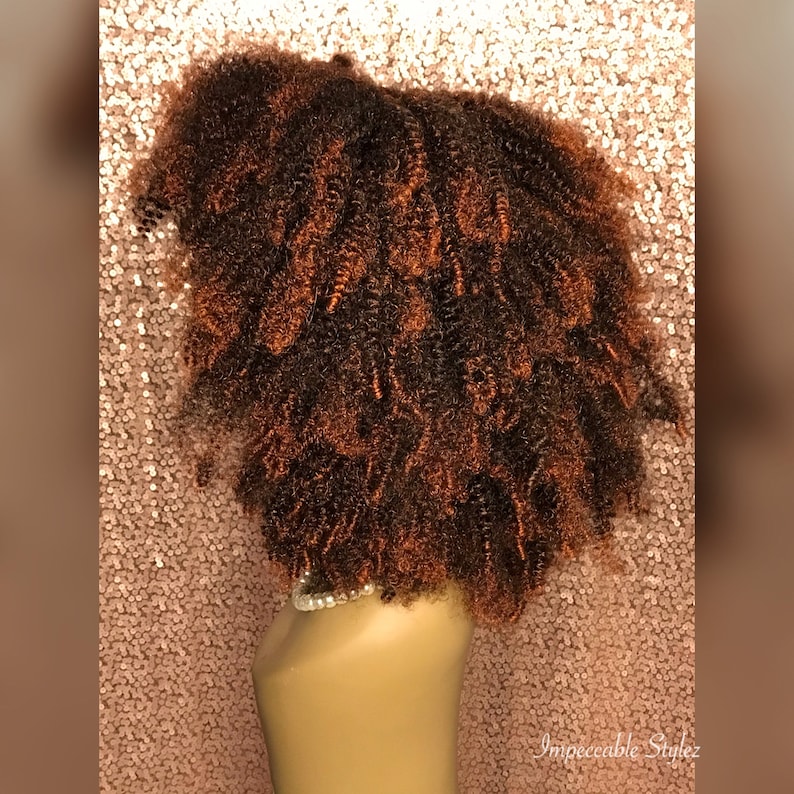 Puede incluir: Una peluca rizada marr&oacute;n y rojiza en una cabeza de maniqu&iacute;. La peluca est&aacute; peinada en un afro corto y voluminoso.