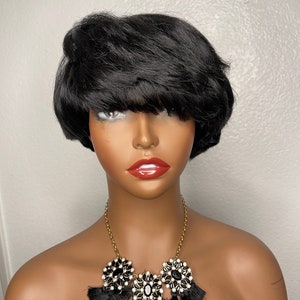 May include: A short black wig with a choppy, layered style. The wig is styled with a side part and has a fringe that falls just above the eyebrows. The wig is worn on a mannequin with a gold necklace featuring black and white rhinestone embellishments.