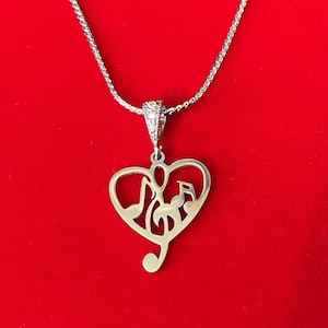 May include: A silver necklace with a heart-shaped pendant featuring a treble clef and musical notes. The necklace is displayed on a red velvet background.