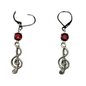 Può includere: Un paio di orecchini d'argento con un cristallo rosso e un ciondolo a forma di chiave di violino.