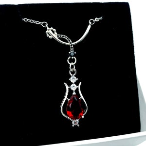Może przedstawiać: Srebrny naszyjnik z czerwonym kamieniem szlachetnym w kształcie tulipana. Zawieszka jest otoczona mniejszymi, przezroczystymi kamieniami.