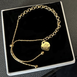 Op de afbeelding: Goudkleurige armband met een hartvormige bedel. De bedel is gegraveerd met de woorden "LOVE FOREVER 520". De armband wordt gepresenteerd in een zwart doosje met witte voering.