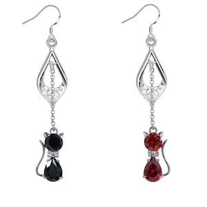 Peut inclure: Une paire de boucles d'oreilles pendantes en argent avec un charme de chat. Le charme de chat est orné d'une pierre précieuse noire ou rouge. Les boucles d'oreilles ont un design délicat et ajouré.