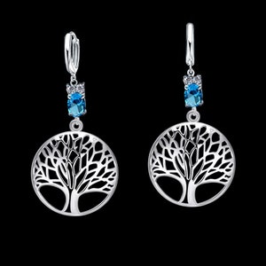 Op de afbeelding: Zilveren oorbellen met een boom des levens ontwerp en een blauwe edelsteen accent.