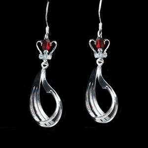 May include: Silver dangle earrings with a red crystal crown at the top and a twisted silver design.