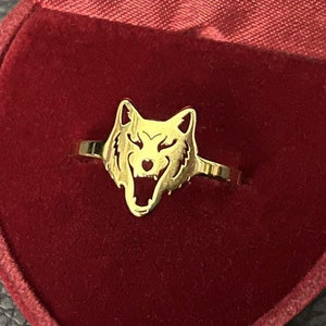 Könnte beinhalten: Ein goldfarbener Ring mit einem Wolfskopf-Design, präsentiert in einer roten Samt-Herzform-Box.
