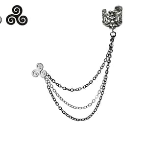 May include: A silver ear cuff with a chain attached to a silver triple spiral charm. The chain is made of two different types of metal, one silver and one black.