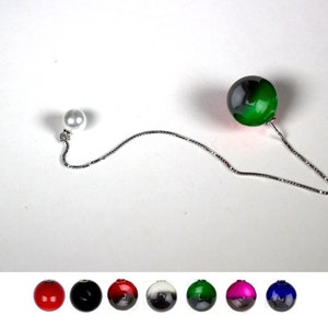 May include: A silver chain with a white pearl on one end and a black and green glass sphere on the other end. The chain is hanging from a white surface. Below the chain are eight different coloured glass spheres: red, black, red and black, black and white, green and black, pink and black, and blue and black.