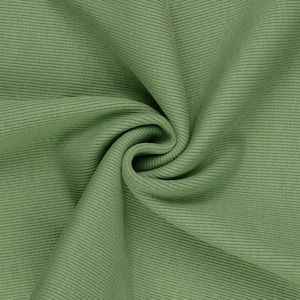 May include: Close-up of a sage green ribbed fabric. The fabric is folded and draped, creating soft shadows and highlighting the texture. The material appears to be a medium weight, suitable for clothing or home decor.