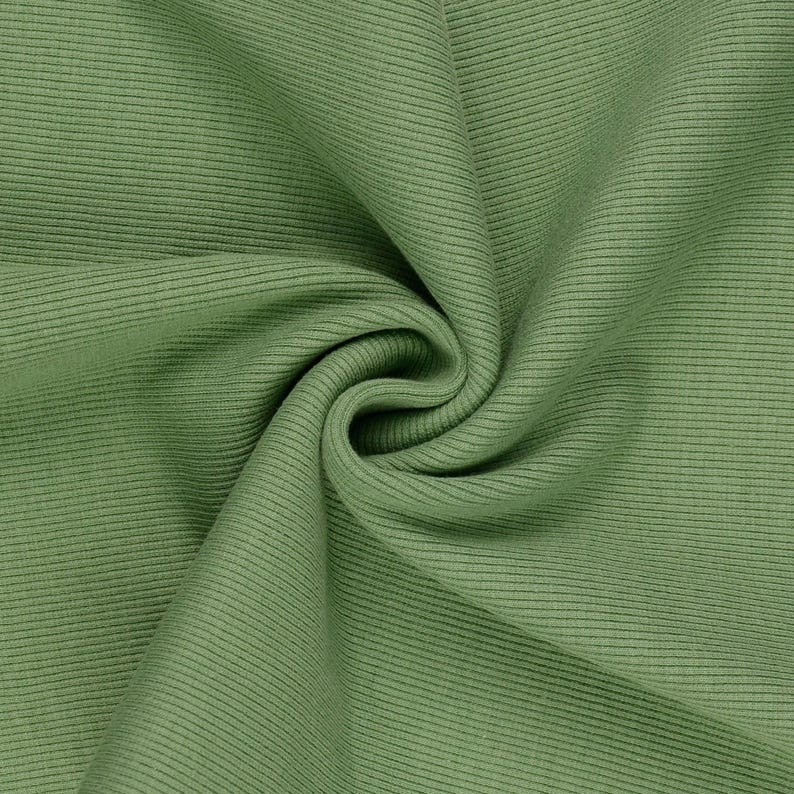 May include: Close-up of a sage green ribbed fabric. The fabric is folded and draped, creating soft shadows and highlighting the texture. The material appears to be a medium weight, suitable for clothing or home decor.