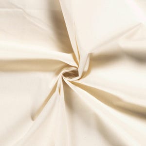 Könnte beinhalten: Nahaufnahme eines cremefarbenen Stoffes mit einem Wirbelmuster. Der Stoff ist in der Mitte zusammengezogen, wodurch ein Spiraleffekt entsteht. Die Falten erzeugen Schatten und Lichtreflexe und verleihen dem Bild Tiefe und Textur. Der Stoff wirkt weich und glatt.
