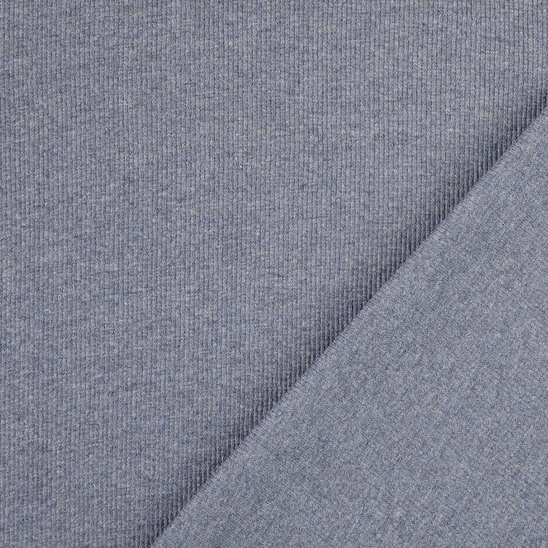 May include: Close-up of a textured, blue-grey fabric. The fabric is ribbed with vertical lines, and a diagonal section of the fabric is visible, showing a smoother texture. The material appears to be a knit or jersey.