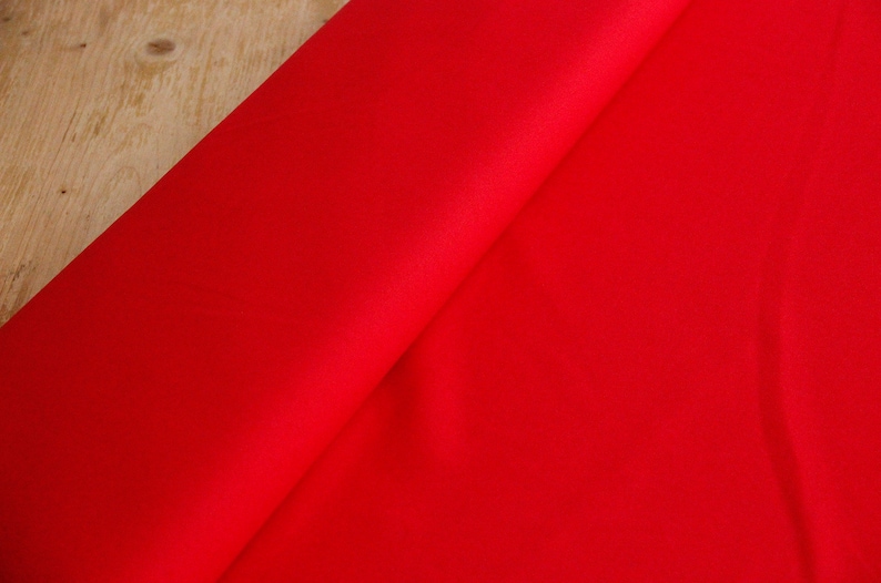 May include: A close-up of a bright red fabric, folded in half, showing the smooth texture of the material.