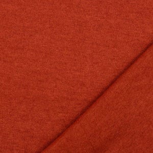 May include: Close-up of a textured, rust-colored fabric. The fabric is folded diagonally, creating a contrast in texture and shadow. The material appears soft and possibly suitable for clothing or home decor.