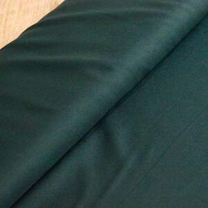 May include: A close-up of a dark green fabric with a smooth texture. The fabric is folded in half, showing the inside and outside of the material.