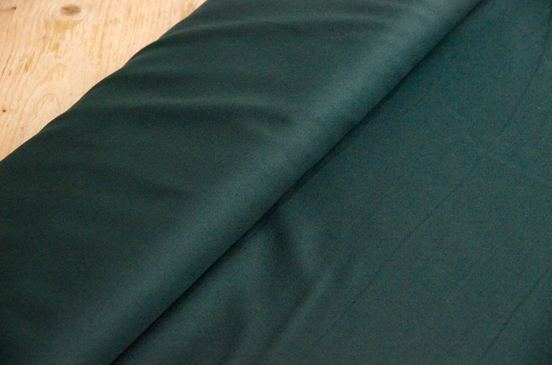 May include: A close-up of a dark green fabric with a smooth texture. The fabric is folded in half, showing the inside and outside of the material.