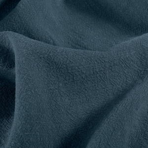 May include: Close-up of a textured, dark teal fabric. The material is folded, showing the weave and subtle variations in color. The fabric appears soft and possibly linen or a similar natural fiber.