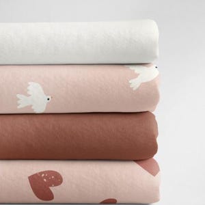 May include: A stack of four fabric swatches in different colors and patterns. The top swatch is white, the second is pink with white doves, the third is brown, and the bottom is pink with brown hearts.