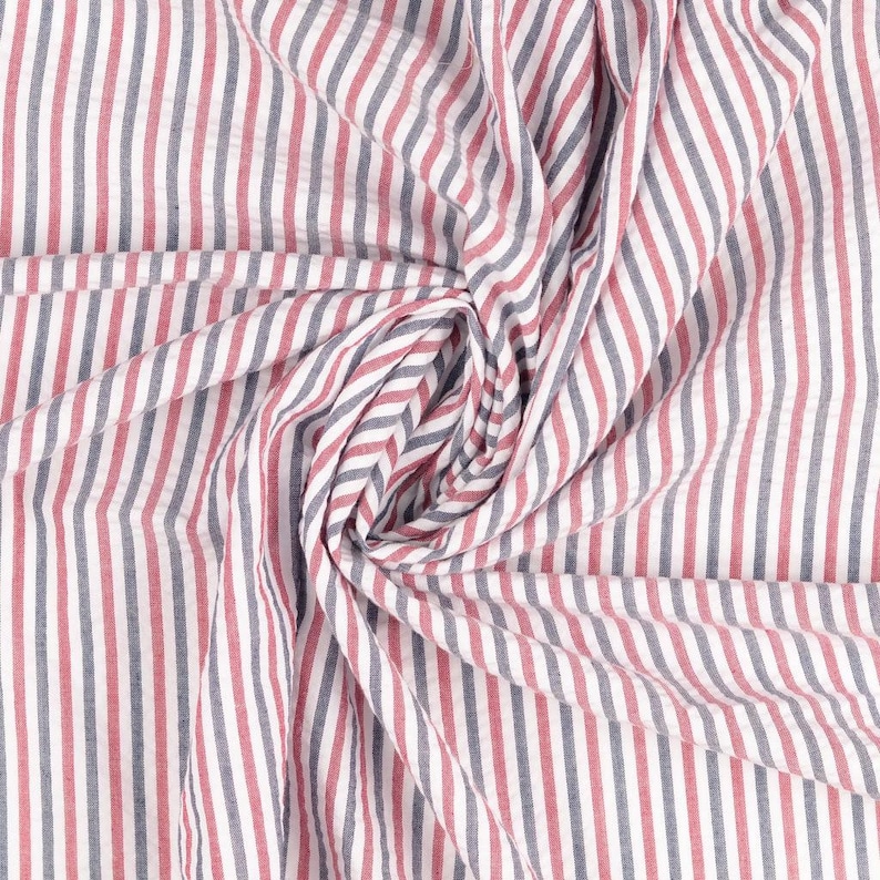Puede incluir: Tela blanca con rayas rojas y azules. La tela est&aacute; doblada y retorcida, creando un patr&oacute;n de remolino.