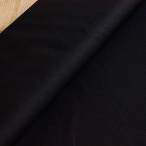 May include: Black fabric with a smooth, even texture. The fabric is folded in half, with one side slightly overlapping the other.