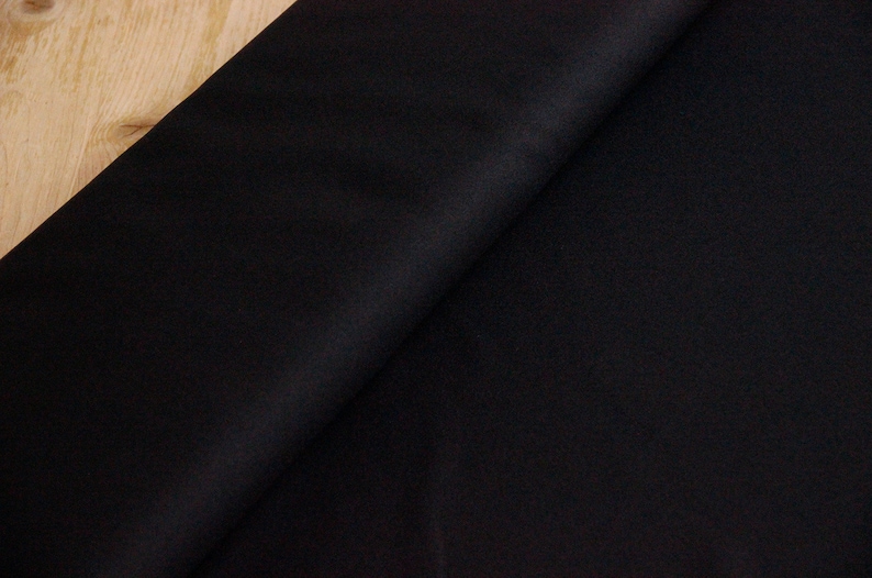 May include: Black fabric with a smooth, even texture. The fabric is folded in half, with one side slightly overlapping the other.