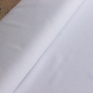 May include: A white fabric with a smooth texture. The fabric is folded in half and the edges are visible.
