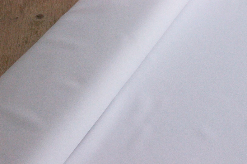 May include: A white fabric with a smooth texture. The fabric is folded in half and the edges are visible.