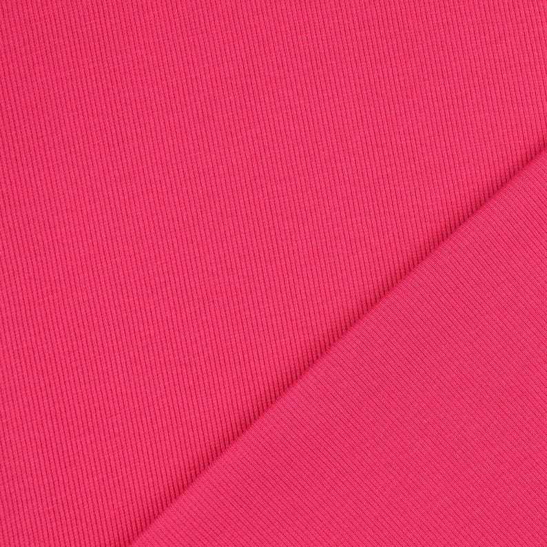 May include: Close-up of a vibrant pink fabric with a ribbed texture. The material is folded diagonally, creating two distinct sections. The color is a bright, solid pink, and the fabric appears to be soft and flexible.