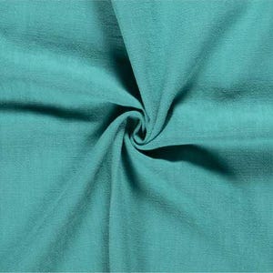 May include: Close-up of a teal fabric with a textured surface. The fabric is gathered in a swirl, creating shadows and highlighting the material's folds. The color is a vibrant, solid teal.