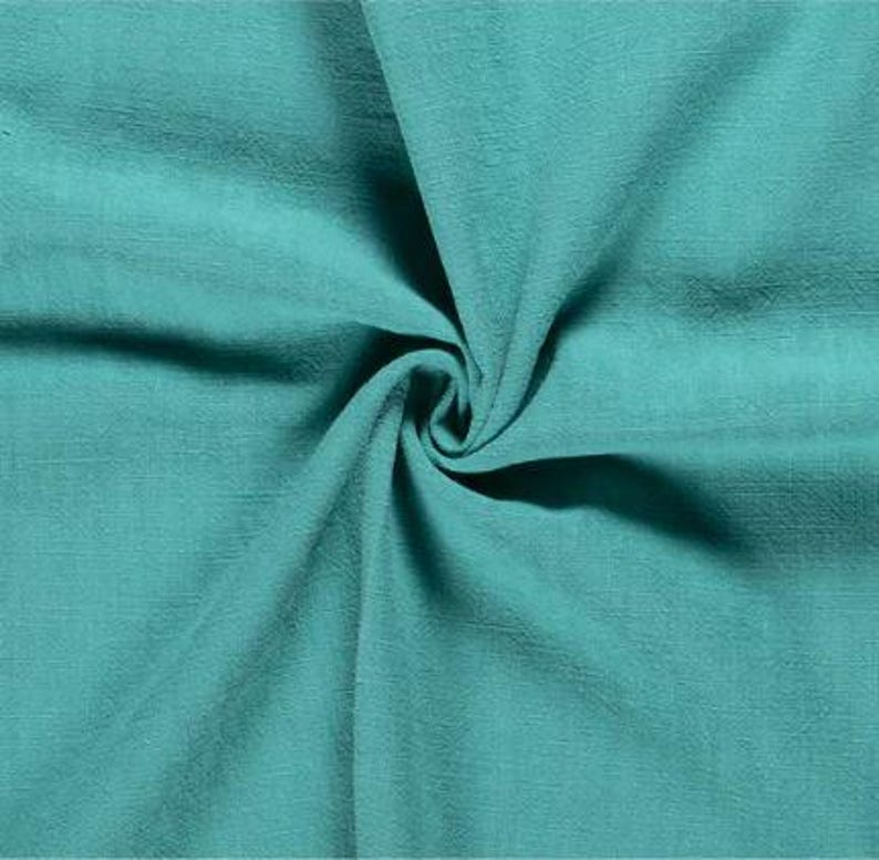 May include: Close-up of a teal fabric with a textured surface. The fabric is gathered in a swirl, creating shadows and highlighting the material's folds. The color is a vibrant, solid teal.