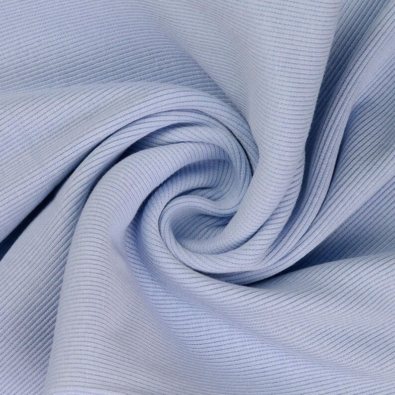 May include: Close-up of a light blue ribbed knit fabric. The fabric is soft and has a textured surface with vertical lines. The fabric is folded and draped, creating shadows and depth.
