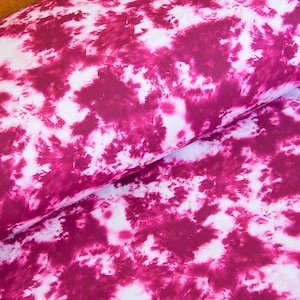 Könnte beinhalten: Weißer Stoff mit einem rosafarbenen Batik-Muster. Der Stoff hat ein wirbelndes, abstraktes Design.