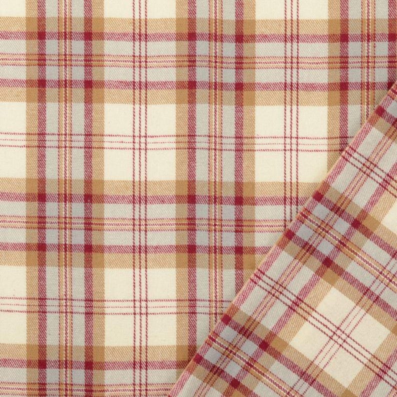 May include: Cream-colored plaid fabric with a pattern of red, tan, and gray lines. The fabric is folded over, revealing the pattern on both sides. The fabric has a woven texture.