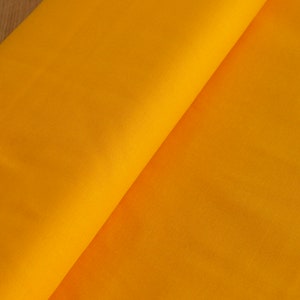 Op de afbeelding: Een close-up van een felgele stof, gevouwen in de helft, die de textuur van het materiaal laat zien.