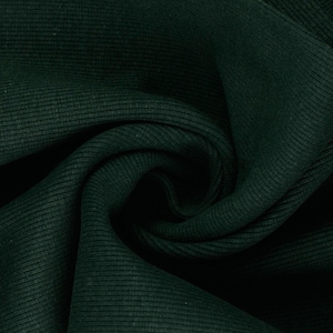 May include: Close-up of dark green ribbed fabric. The fabric has a textured surface with vertical ridges and a slight sheen. The material is folded and draped, creating shadows and depth.
