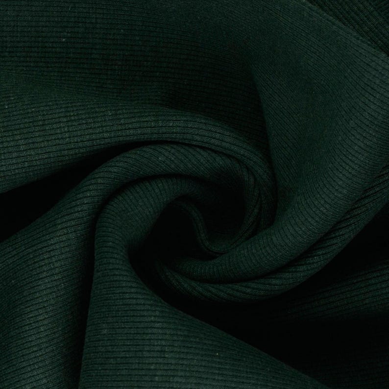 May include: Close-up of dark green ribbed fabric. The fabric has a textured surface with vertical ridges and a slight sheen. The material is folded and draped, creating shadows and depth.